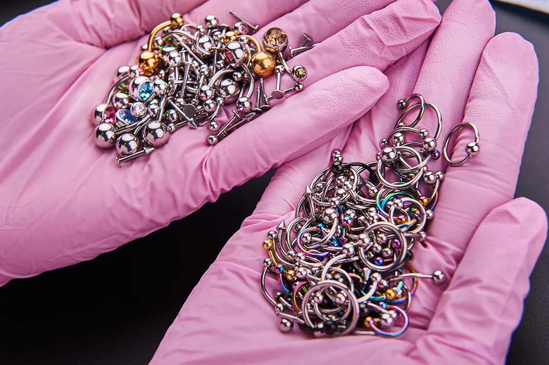 Hände in rosa Medizinhandschuhen halten viele Piercings