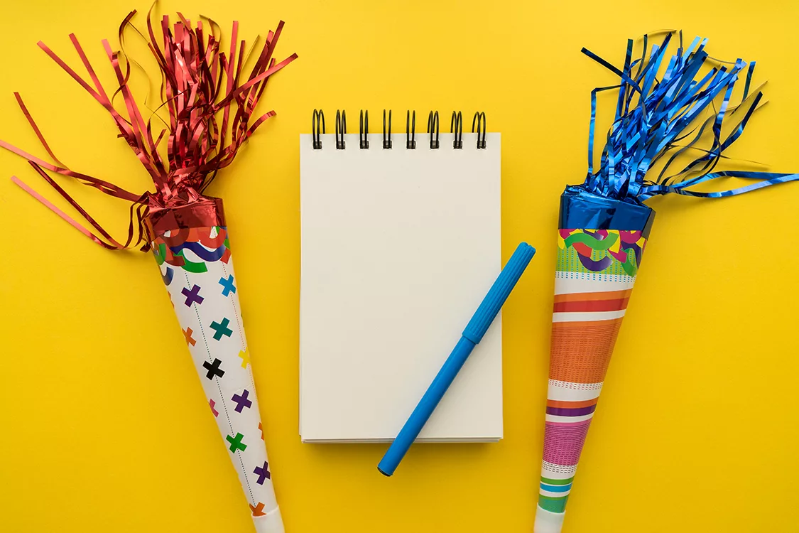 Notizblock mit Stift. Daneben zwei Schultüten. alles auf gelbem Hintergrund