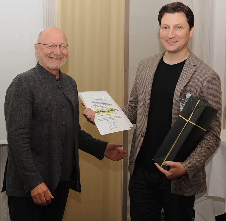 Abbildung. 3: Dr. Bernd Reiss (li.) überreicht die Urkunde an PD Dr. Alexey Unkovskiy, MSc. (Charité Berlin), der als Hauptautor und stellvertretend für das Team einen der beiden AGK+ Forschungspreise entgegennimmt.
