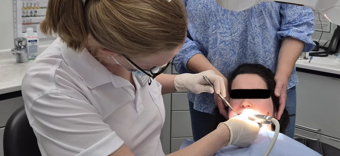 Durchführung einer professionellen Zahnreinigung im Behandlungsstuhl bei derselben jungen erwachsenen Patientin mit Rett-Syndrom nach Umlagerung aus dem eigenen Rollstuhl.
