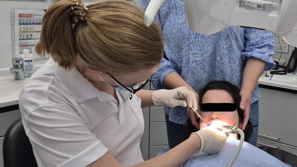 Durchführung einer professionellen Zahnreinigung im Behandlungsstuhl bei derselben jungen erwachsenen Patientin mit Rett-Syndrom nach Umlagerung aus dem eigenen Rollstuhl.