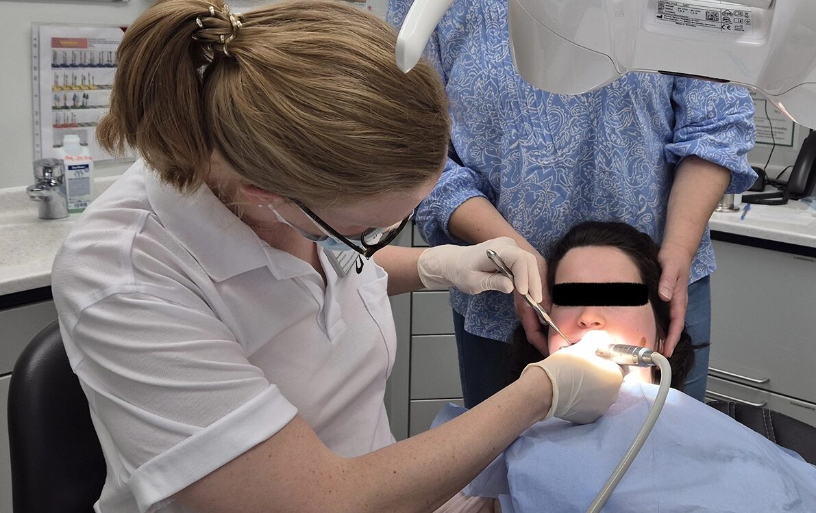 Durchführung einer professionellen Zahnreinigung im Behandlungsstuhl bei derselben jungen erwachsenen Patientin mit Rett-Syndrom nach Umlagerung aus dem eigenen Rollstuhl.