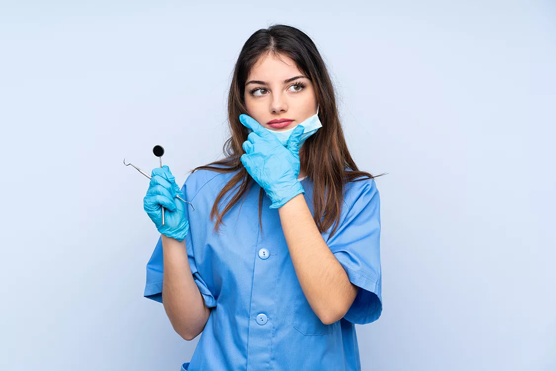 Woman dentist holding tools over isolated blue background thinking an idea