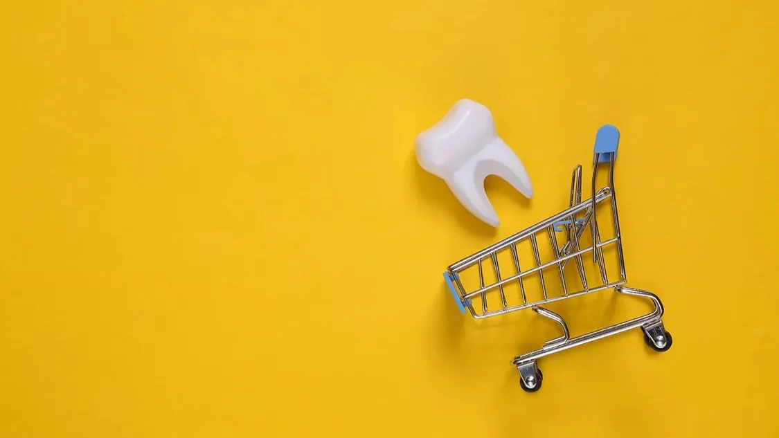 gefalschter-zahn-im-einkaufswagen-auf-gelbem-hintergrund-ansicht-von-oben