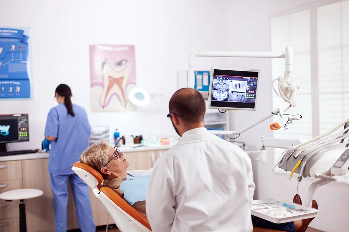 Senior woman discussing with dentist in dental cabinet about teeth issue sitting on chair. Medical teeth care taker discussing with senior woman about mouth hygiene.