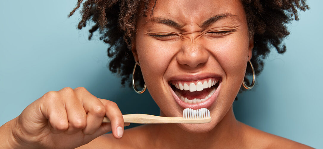 Lachende Frau mit dunklen Locken und einer Handzahnbürste in der Hand