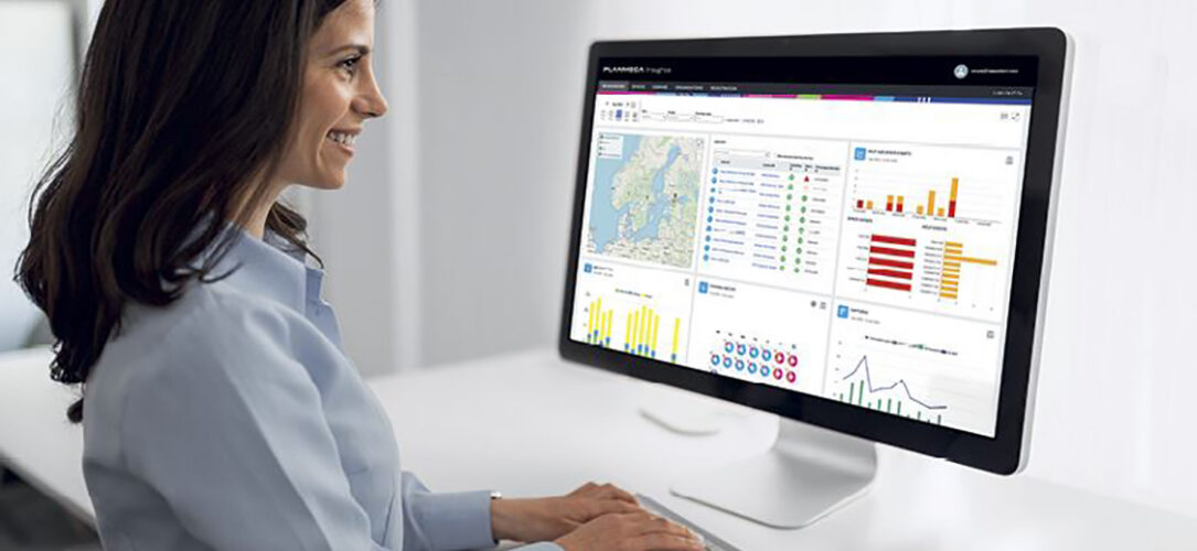 Planmeca Insights Lächelnde Frau sitzt vor PC Bildschirm und arbeitet.