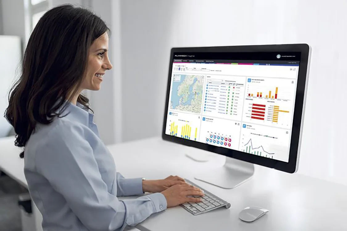 Planmeca Insights Lächelnde Frau sitzt vor PC Bildschirm und arbeitet.