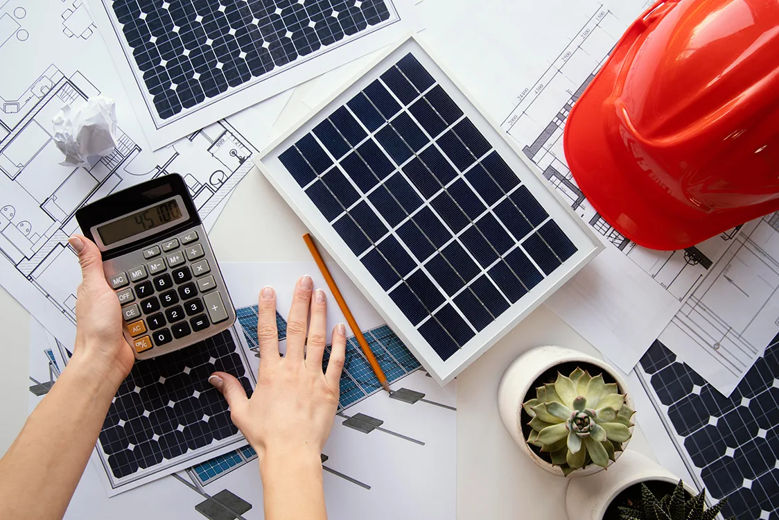 Solarzellen, Taschenrechner, roter Helm, Unterlagen zur Planung auf einem Tisch