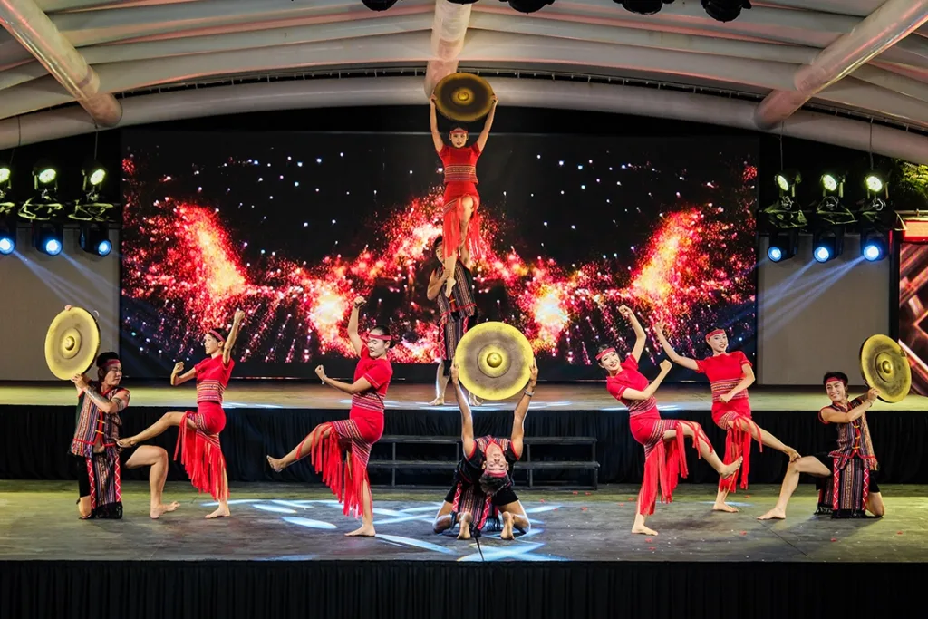 Darsteller in roten Kostümen, im Hintergrund eine Feuershow.