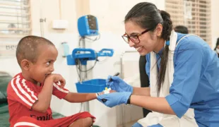 Eine fröhliche Interaktion in einem Behandlungszimmer zwischen einem Kleinkind und ärztlichem Personal.