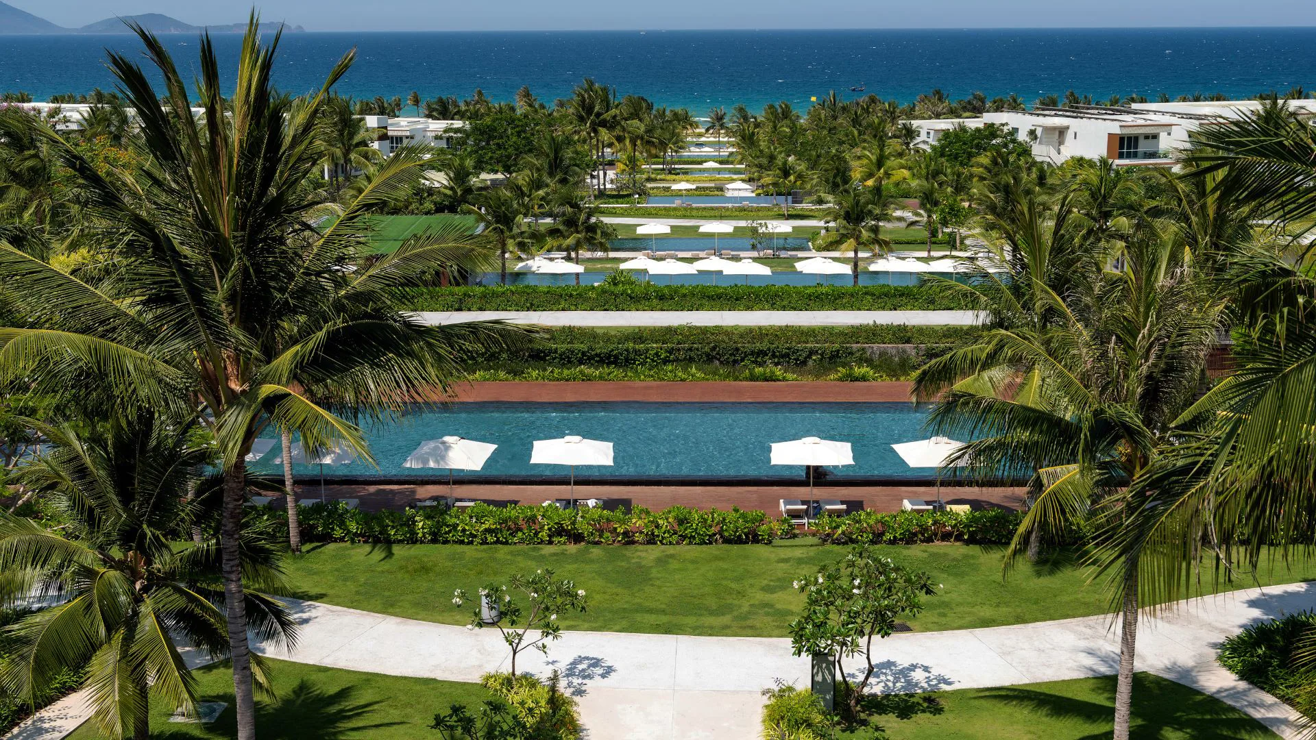 Ein Resort mit Aufsicht aufs Meer. Im Vordergrund Palmen und Sonnenschirme.