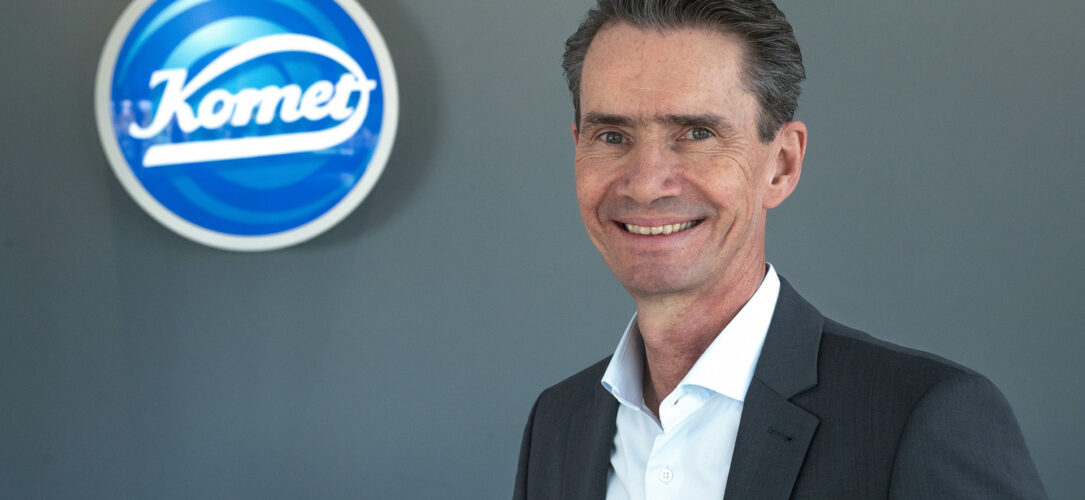 Klaus Rübesamen lächelnd vor dem Komet Dental Logo.