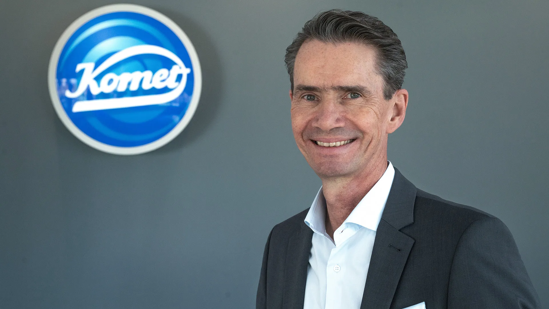 Klaus Rübesamen lächelnd vor dem Komet Dental Logo.