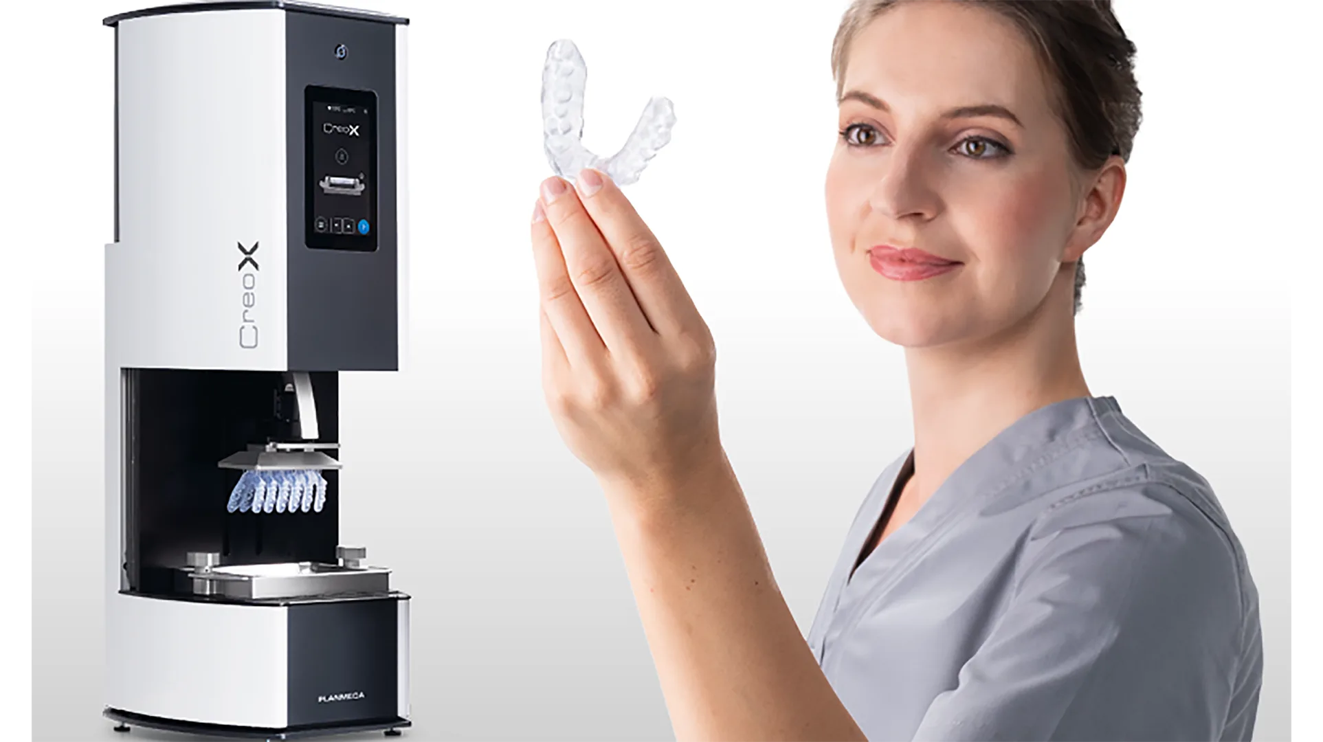 Planmeca Creo® X und daneben eine Frau, die eine Aufbissschiene in der Hand hält.