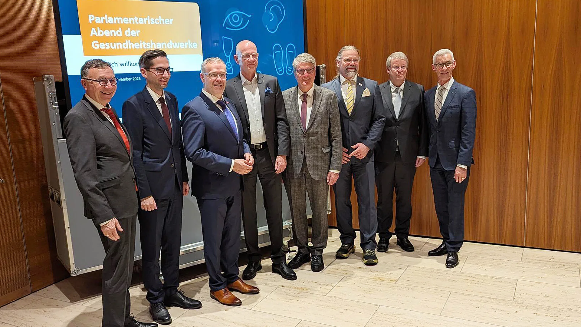Eine Gruppe von Männern in Anzügen stehen vor einer Leinwand mit folgendem Titel: Parlamentarischer Abend der Gesundheitshandwerke