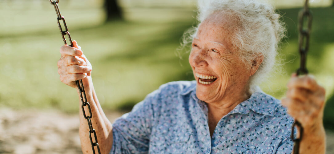 Cheerful senior woman on a swing at a playground