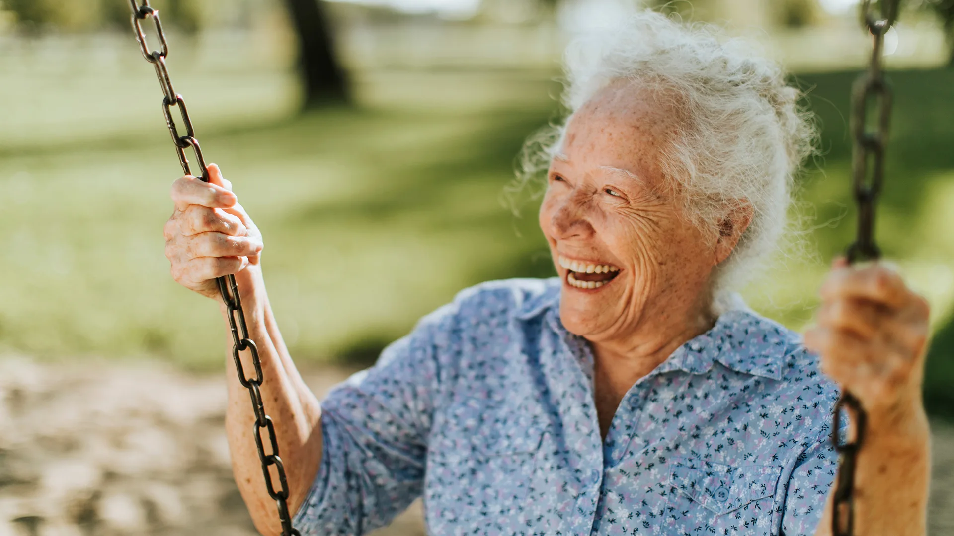 Cheerful senior woman on a swing at a playground