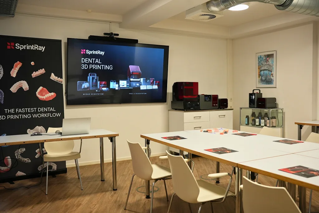 Ein Meetingraum mit einem Bildschirm und einem Plakat für Dental 3D Printing.