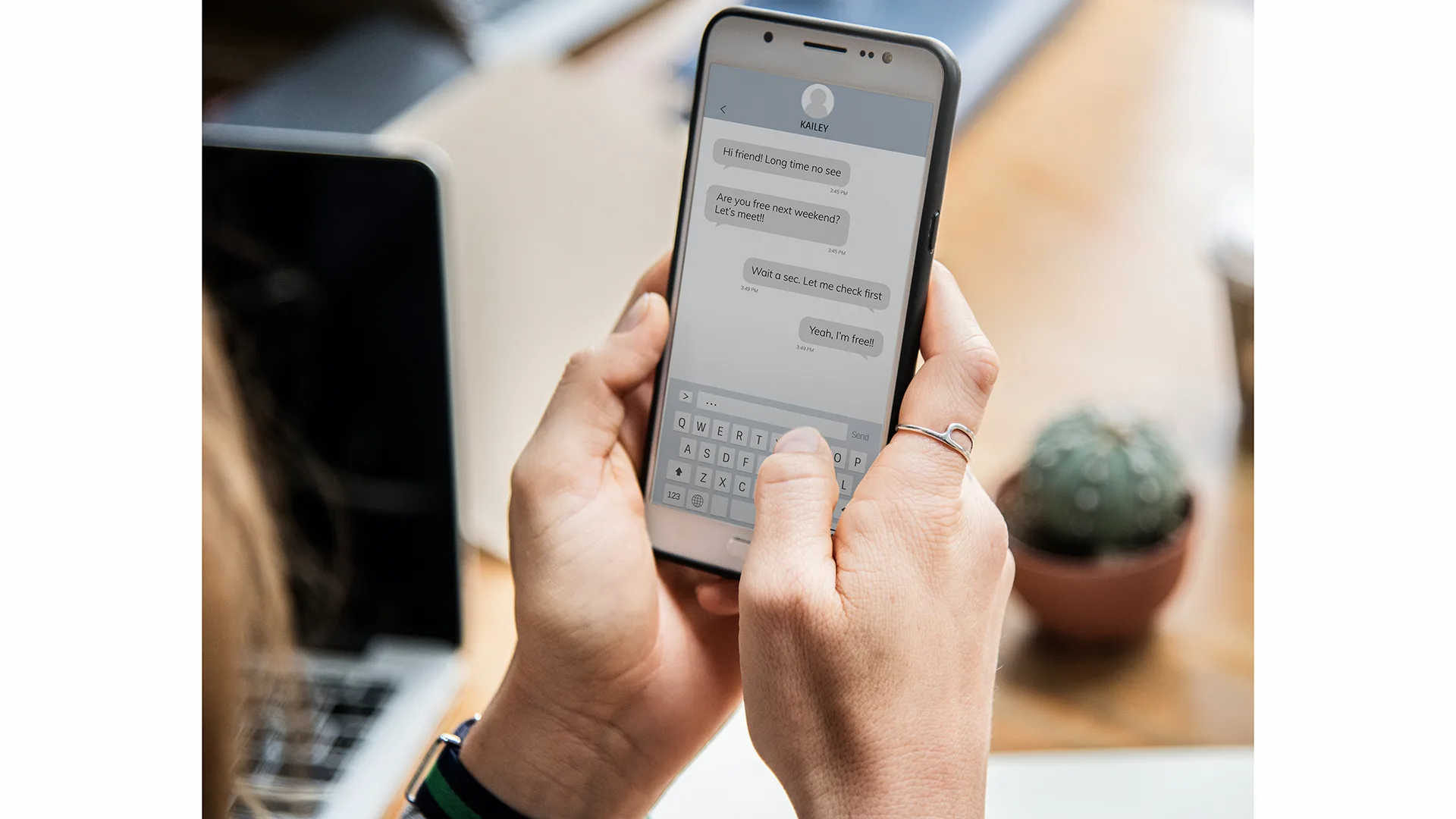 Frau nutzt Whatsapp am Handy. Im Hintergrund sieht man einen Schreibtisch mit Laptop und Kaktus.
