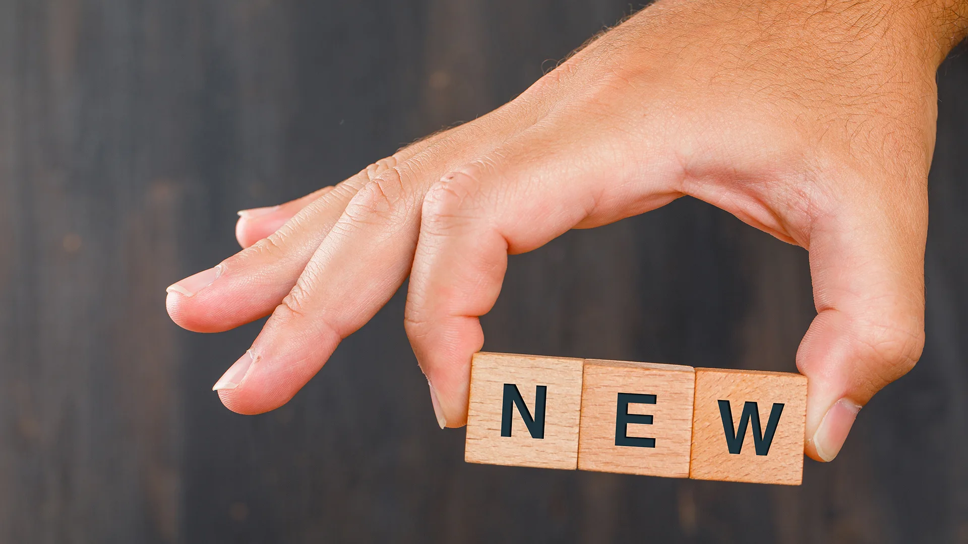 Eine Hand hält drei Bausteine aus Holz, die zusammen das Wort new bilden.