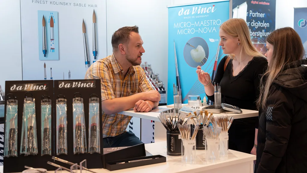 Ein Mann und zwei Frauen unterhalten sich an einem Messestand