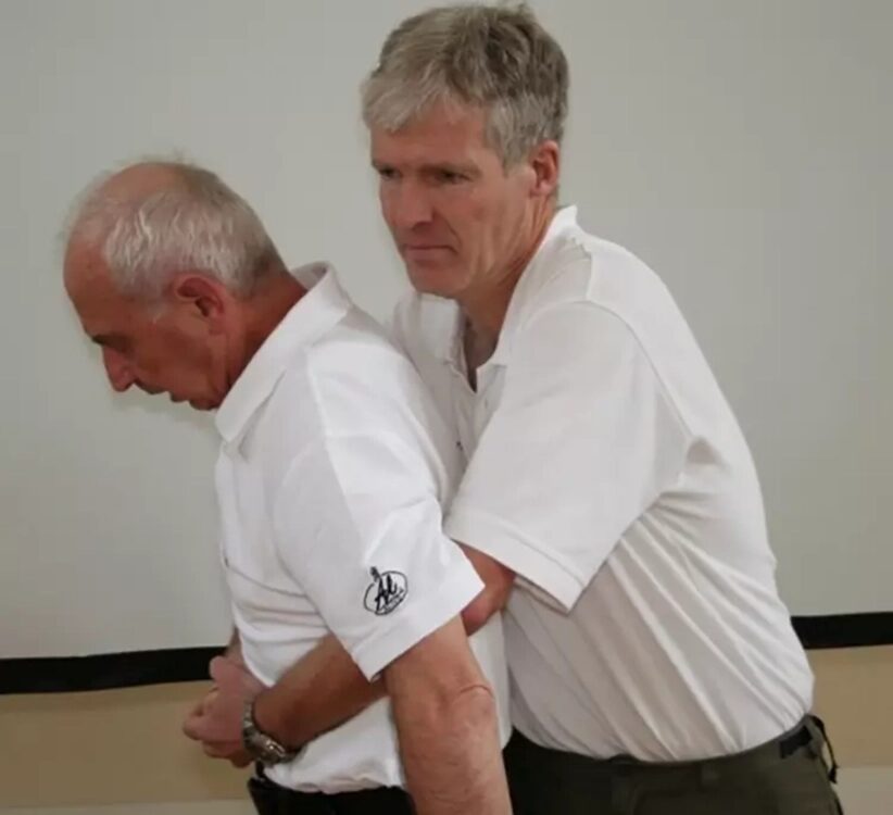 Ein Mann hält einen anderen am Bauch fest und umschlingt ihn dabei von hinten