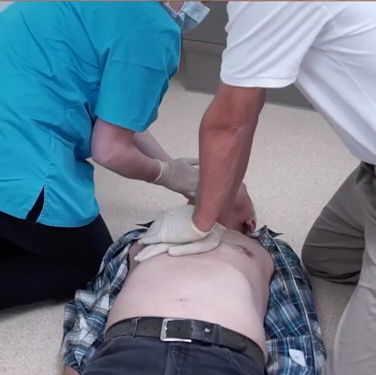 Ein Mann liegt am Boden, zwei weitere wollen ihn reanimieren