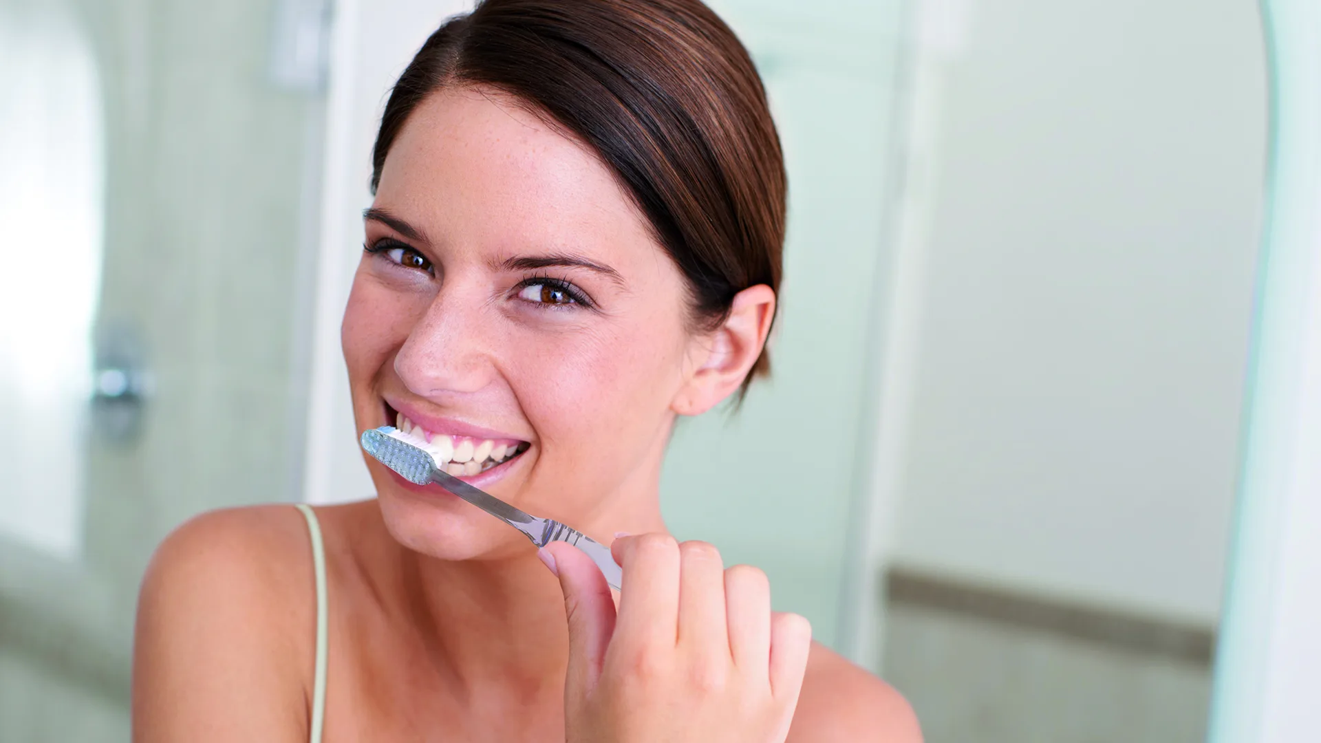 Eine Frau die sich lachend die Zähne putzt.