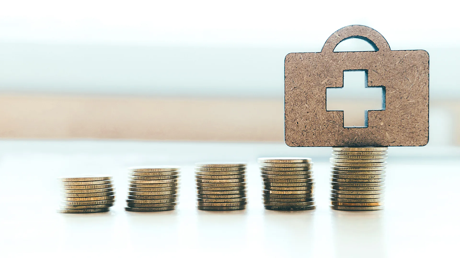 mehrere Kleingeldstapel und auf dem letzten Stapel ein Krankenkoffer.