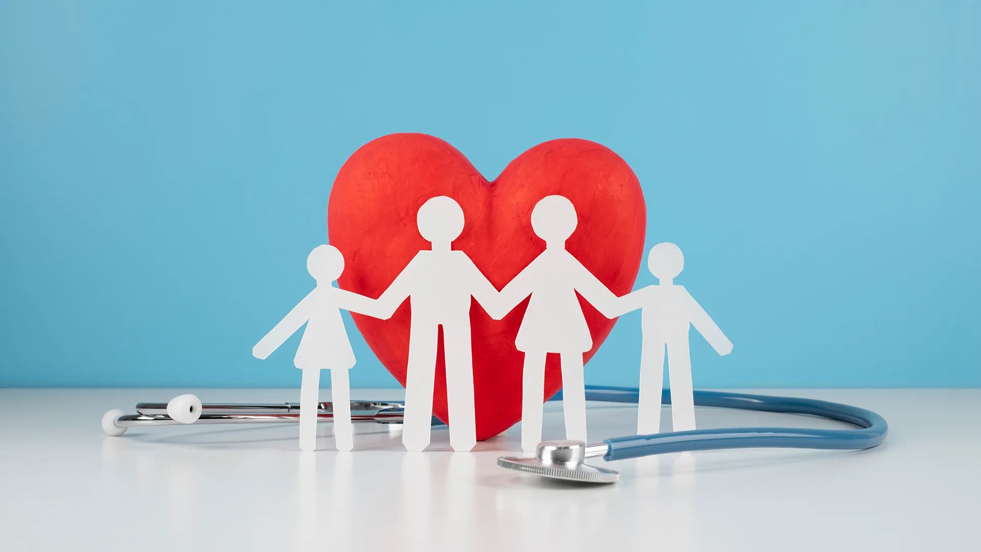 Ein Herz und davor Papierfiguren einer Familie.