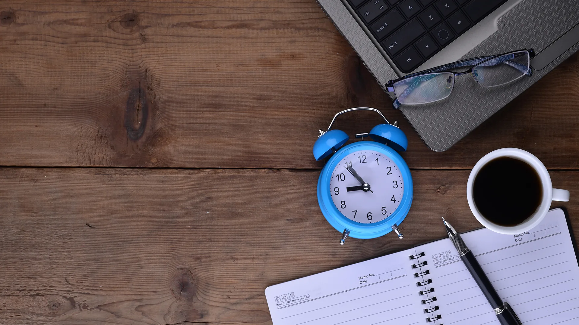 Arbeitsplatz mit einem Laptop, einer Uhr, einem Kaffee und einem Notebook.