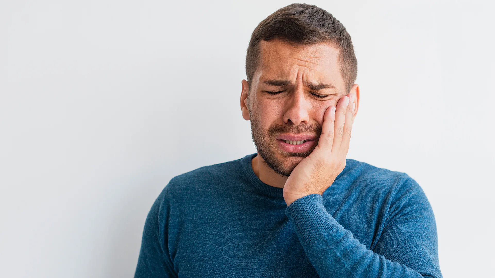 Ein Mann hat Schmerzen und hält sich die Hand an die Wange.
