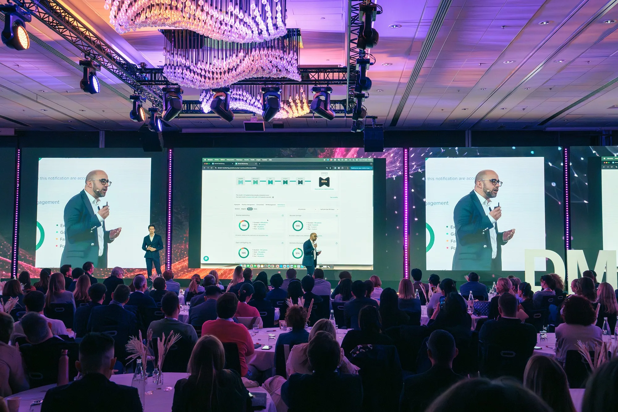 Viele Menschen hören in einem Saal einem auf einer Bühne stehenden Referenten bei seinem Vortag zu.