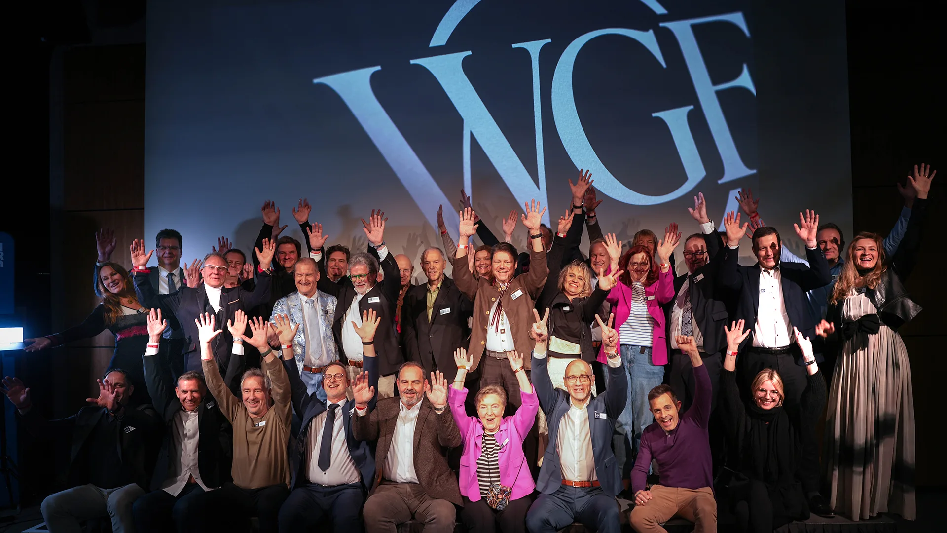 Gruppe von Menschen posiert for dem Logo und hebt die Hände in die Luft.