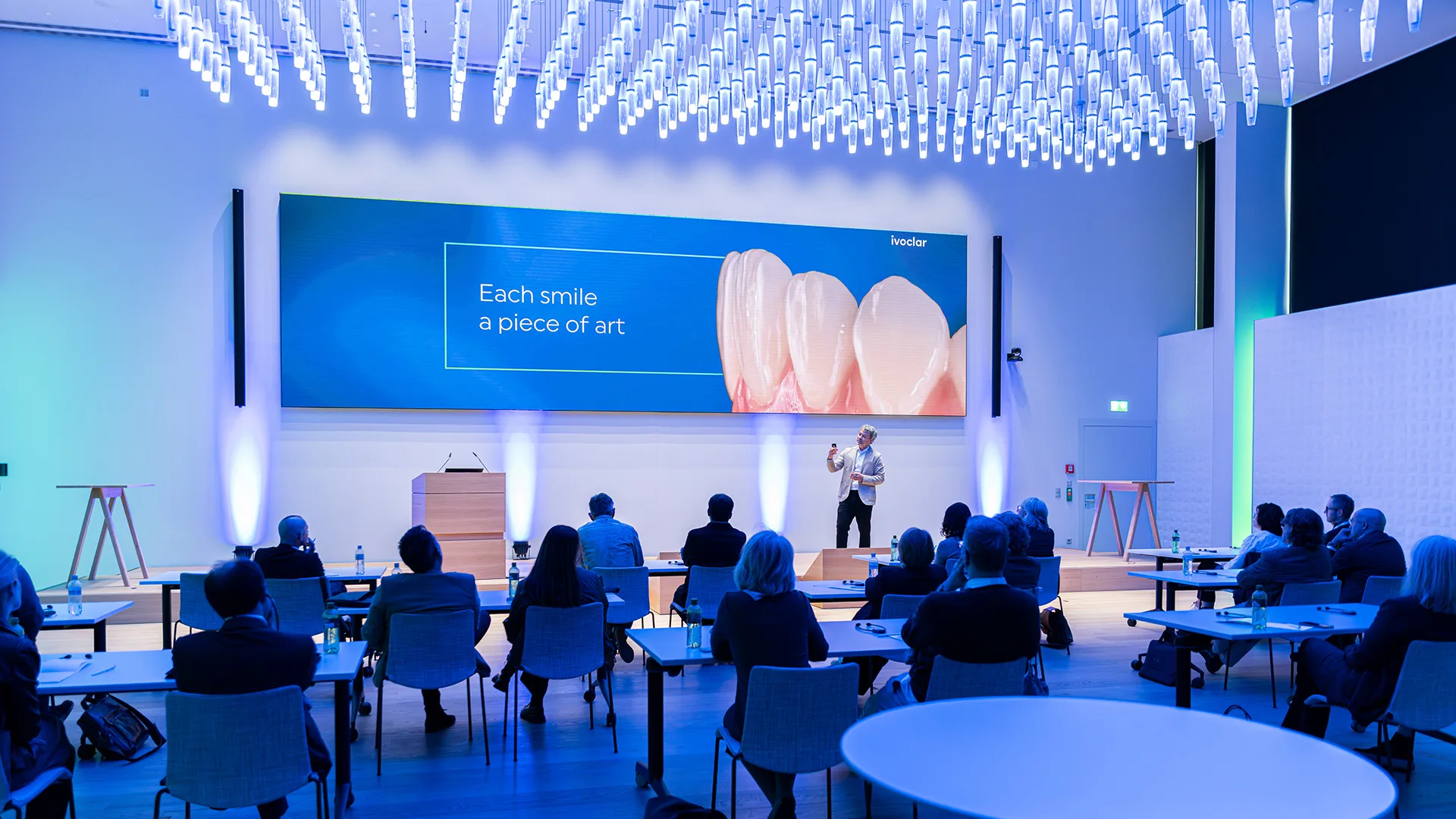 In einem Raum wird ein Vortrag gehalten und Menschen hören zu.