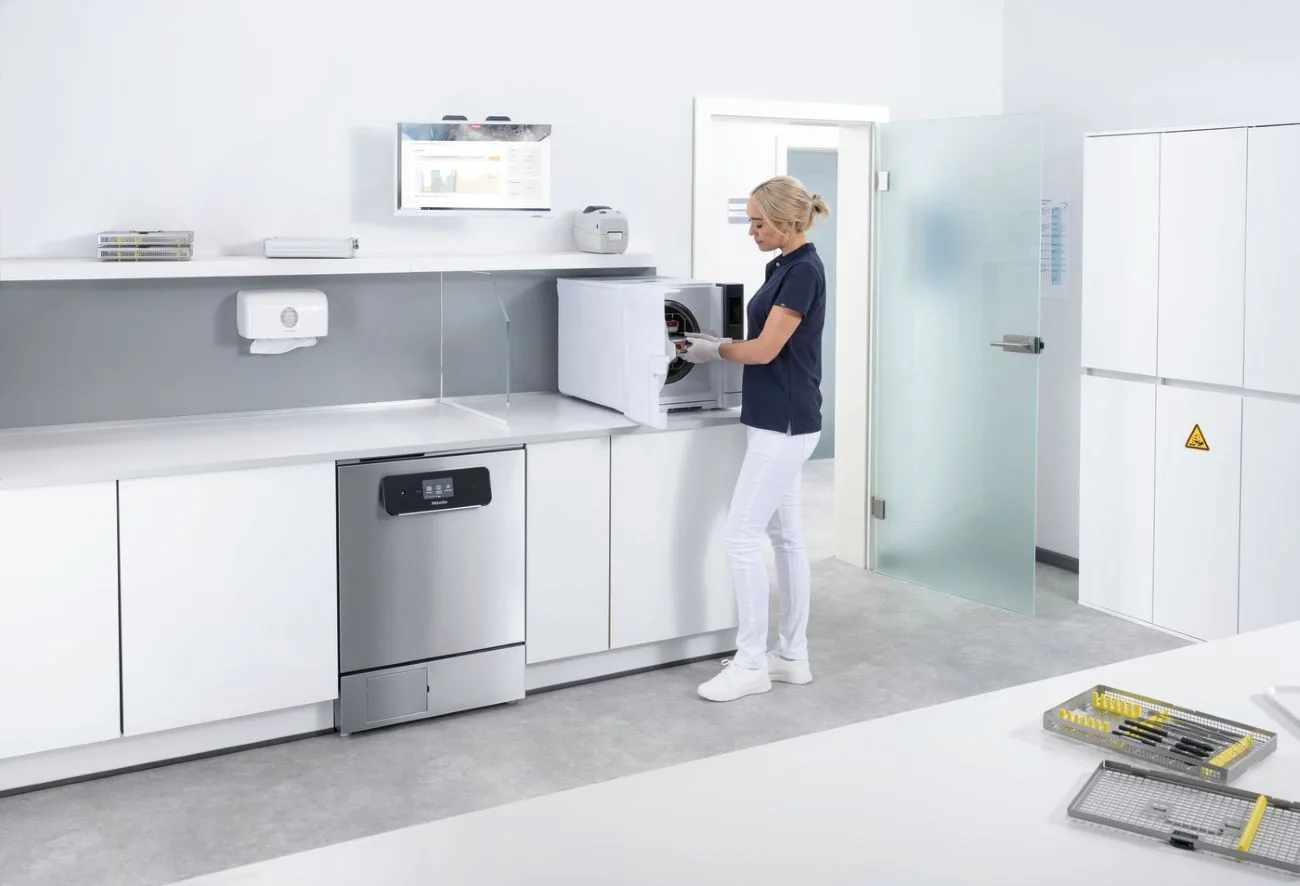 Mitarbeiterin einer Praxis steht in einem großen, v.a. weiß gestalteten Raum und kümmert sich um die Instrumentenaufbereitung.