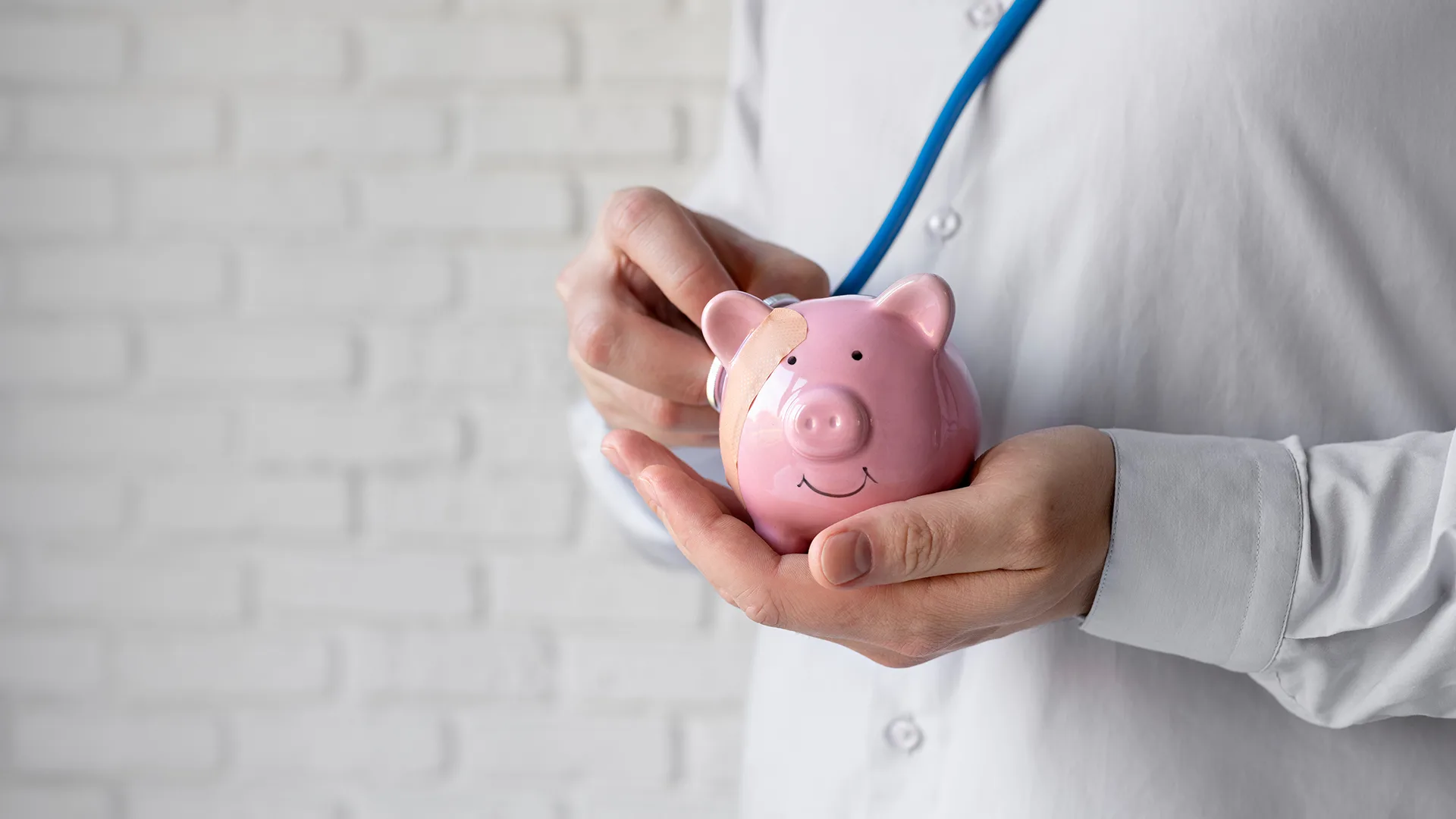 Arzt hält Sparschwein auf dem ein Pflaster geklebt wurde.