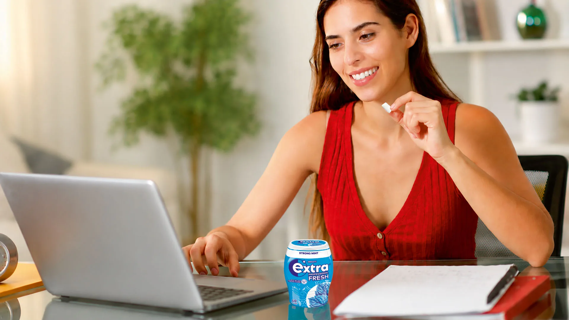 Eine Frau sitzt am Schreibtisch mit ihrem Laptop und hat einen Kaugummi in der Hand.