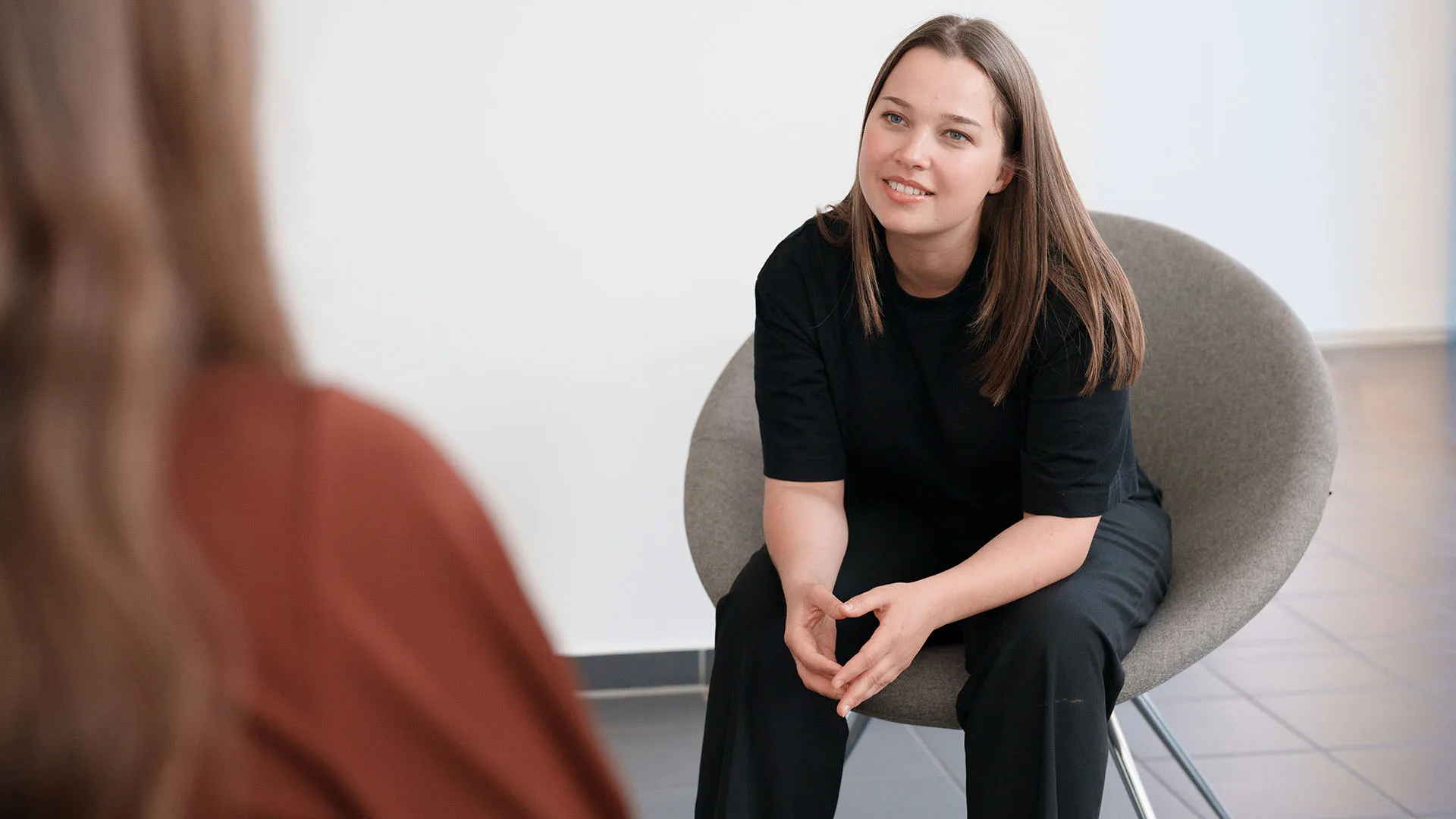Eine Frau sitzt auf einem Stuhl und hört einer anderen zu.
