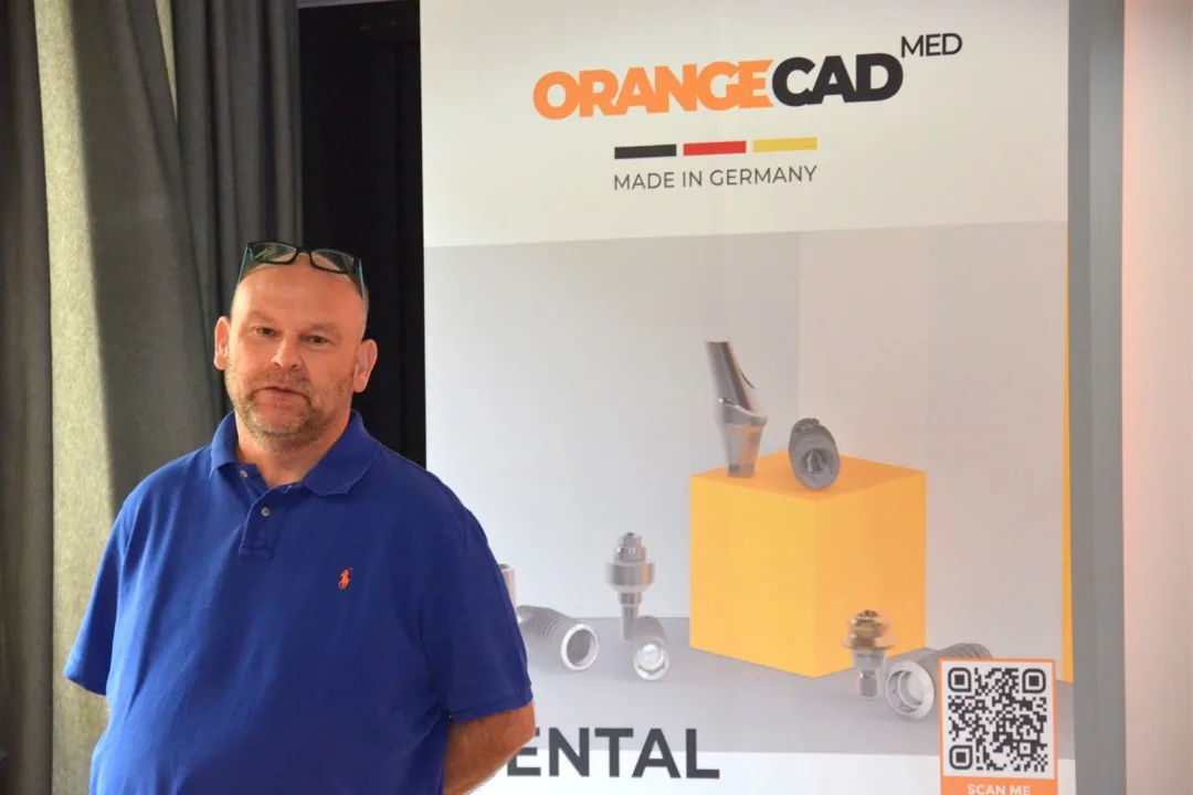 Dr. Andreas Schütt, Gründer und Geschäftsführer von OrangeCAD MED vor dem Firmenlogo.