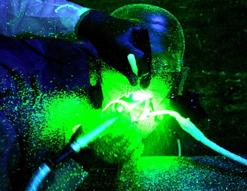 Abb. 1: Aerosol und Spraynebelrückprallbildung im unmittelbaren Umfeld des Patientenmundes während der Anwendung eines maschinellen Scalers am Phantomkopf im verdunkelten Behandlungsraum. (Kühlmedium mit bei Schwarzlicht fluoreszierendem Natriumsalz versetzt nach digitaler Bearbeitung des Bildes mit einer Grafiksoftware).