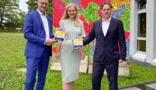V.l.n.r. M. Dürrstein (CEO), M. Jakubaschk (HR Business Partner) & C. Melloh (Director HR & Legal) mit dem kununu-Award vor dem neuen Pop-Art-Kunstwerk auf einer Original Berliner Mauer, das vor der Technischen Akademie von Dürr Dental steht.