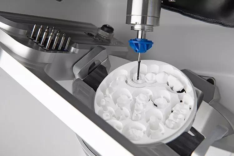 Bearbeitung einer Zirkonronde mit dem zum Patent angemeldeten AIRTOOL, das entstehende Späne vom Werkstück wegbläst. Im Hintergrund: der Werkzeugwechsler mit Platz für 16 Werkzeuge und ein AIRTOOL.