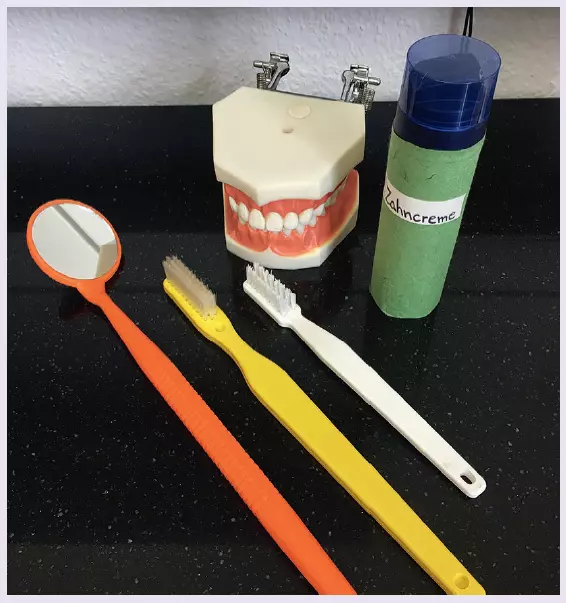 Abb. 3: Zahnmodell mit großen Zahnbürsten, Mundspiegel und Rasierschaum als Zahncreme für die Putzübung des Kindes.