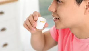 Junger Mann mit Mundspüllösung in der Praxis.